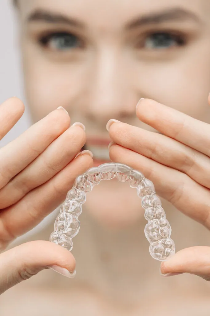 Una mujer usa un entrenador ortodóntico de silicón para corregir sus dientes. Este dispositivo móvil muestra los métodos modernos de cuidado dental y los sistemas de blanqueamiento, y promueve una sonrisa sana y radiante.