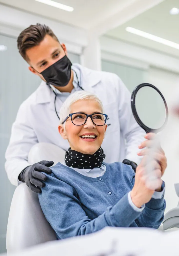 Una hermosa mujer mayor recibe tratamiento dental en el consultorio del dentista. El dentista usa mascarilla protectora debido a la pandemia de coronavirus.