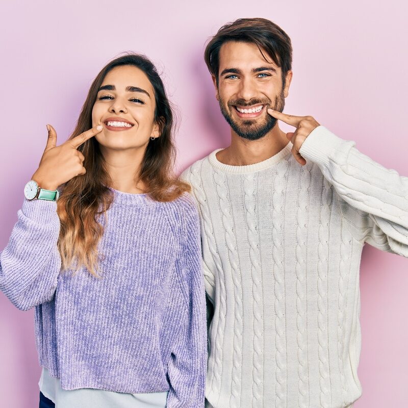 Young hispanic couple wearing casual clothes smiling cheerful showing and pointing with fingers teeth and mouth. dental health concept.